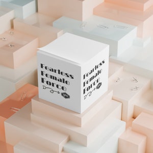 May include: White notepad with the text "Fearless Female Force" written in black. The notepad is sitting on a stack of light pink and light blue boxes.