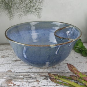 Könnte beinhalten: Eine handgefertigte blaue Keramik-Servierschüssel mit integriertem Dip-Bereich. Die Schüssel hat eine rustikale, glasierte Oberfläche mit braunen Rändern. Die Schüssel eignet sich perfekt zum Servieren von Snacks und Vorspeisen. Die Schüssel hat einen Durchmesser von ca. 30 cm.