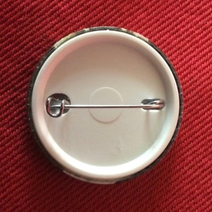 May include: The back of a round button with a silver pin and a white background.
