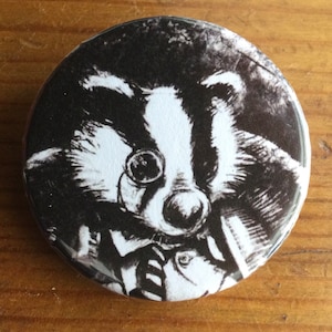 May include: A black and white button with a cartoon badger wearing a monocle and a bow tie. The badger is looking directly at the viewer.