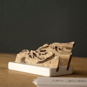 May include: A wooden business card holder with a unique, natural, and organic design. The holder is made of a single piece of wood with a natural, rustic finish. The holder is sitting on a wooden surface.