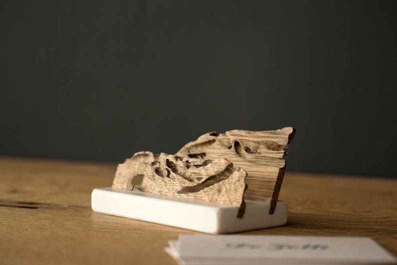 May include: A wooden business card holder with a unique, natural, and organic design. The holder is made of a single piece of wood with a natural, rustic finish. The holder is sitting on a wooden surface.