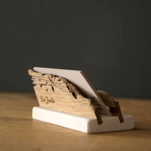 May include: A wooden business card holder with a natural wood finish. The holder is shaped like a mountain range and has a white base. The text "Del Solli" is engraved on the front of the holder.