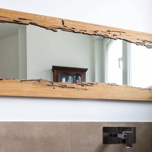 May include: A rectangular mirror with a natural wood frame. The frame has a unique, rustic design with knots and cracks in the wood. The mirror is hanging on a white wall.