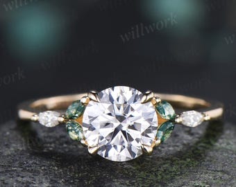 May include: A gold ring featuring a large round brilliant-cut center stone, flanked by two marquise-cut green moss-like stones and two smaller marquise-cut clear stones on each side, set on a thin polished gold band.