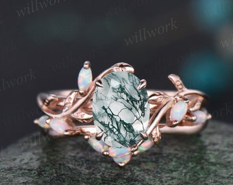 May include: Rose gold engagement ring with a green moss agate center stone and a delicate leaf design. The ring is set with smaller white opal stones on the band.