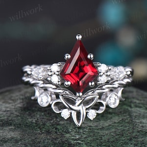May include: A silver ring with a large, red, square-shaped gemstone surrounded by smaller, white gemstones. The ring features a Celtic knot design.
