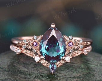 Op de afbeelding: Een verlovingsring van roségoud met een peervormige alexandriet-edelsteen, omringd door kleinere diamanten en roze saffieren. De ring heeft een delicaat bloemmotief met bladeren en bloemen.