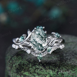 May include: A silver ring featuring a green moss agate gemstone and a delicate leafy design. The ring is set with smaller green stones and diamonds.