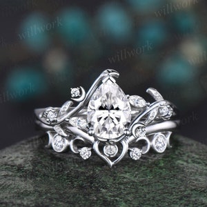 May include: A pear-shaped diamond engagement ring with a delicate floral design. The ring features a pear-shaped center stone surrounded by smaller diamonds and intricate floral details. The ring is set in a white metal band.