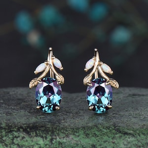 May include: A pair of gold earrings with a blue gemstone and white opal accents. The earrings feature a delicate branch design with leaves.