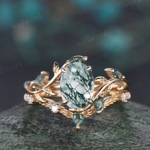 May include: A rose gold engagement ring with a green moss agate center stone and a delicate leaf design. The ring is set with smaller green stones and diamonds.