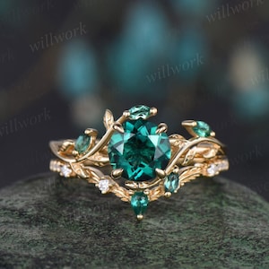 May include: A gold ring with a large emerald green gemstone surrounded by smaller emerald green gemstones. The ring features a delicate, leafy design.