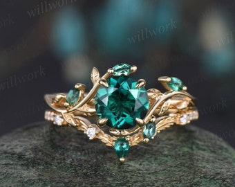 May include: A gold ring featuring a large emerald green gemstone surrounded by smaller emerald green gemstones. The ring has a delicate, leafy design.