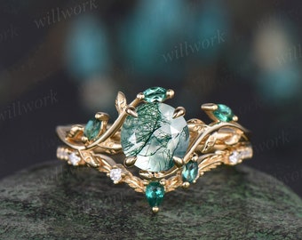 May include: A gold ring featuring a green gemstone set within a leafy design. The ring is embellished with smaller green gemstones.