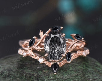 May include: Rose gold engagement ring set with a black rutilated quartz oval gemstone and black diamond accents. The ring features a delicate branch design.