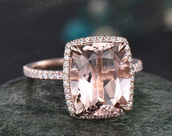 May include: A rose gold engagement ring with a large, cushion-cut morganite center stone surrounded by a halo of smaller diamonds. The band is also set with smaller diamonds.