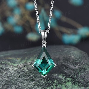 May include: A silver chain necklace with a large, emerald green, faceted gemstone pendant. The pendant is shaped like a diamond and has a pointed tip.