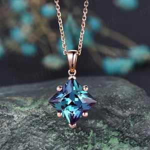 May include: A rose gold chain necklace with a square-shaped pendant featuring a blue and green gemstone.