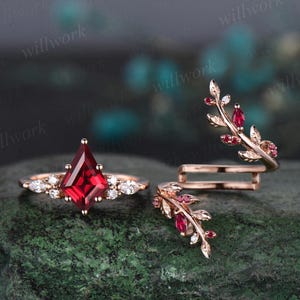 May include: A set of two rose gold rings featuring red gemstones. One ring has a square-shaped red gemstone surrounded by smaller white gemstones. The other ring is a delicate branch design with red gemstones and small white gemstones.