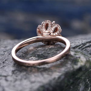 May include: A rose gold engagement ring with a delicate, floral-inspired design. The ring features a center stone surrounded by smaller diamonds, creating a sparkling halo effect.