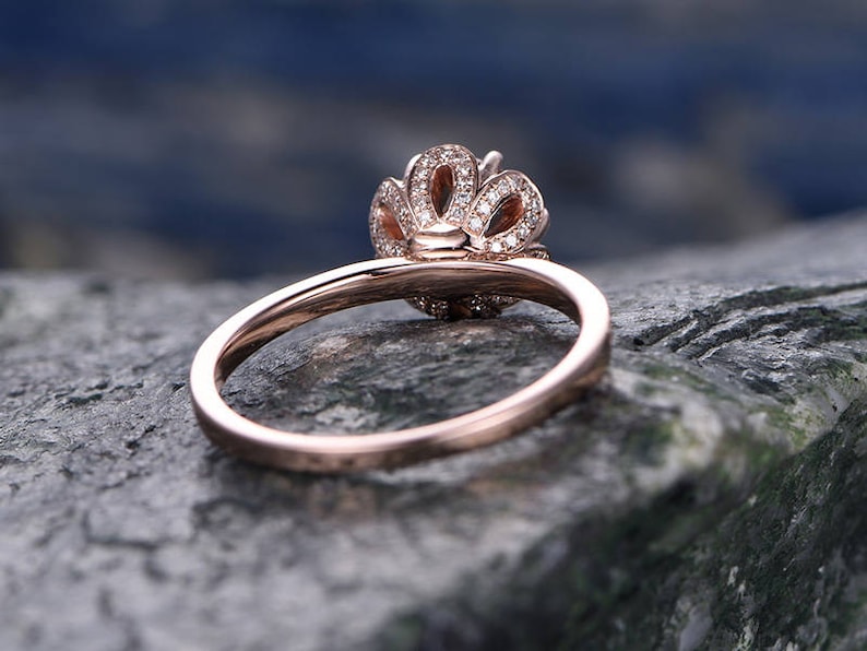 May include: A rose gold engagement ring with a delicate, floral-inspired design. The ring features a center stone surrounded by smaller diamonds, creating a sparkling halo effect.
