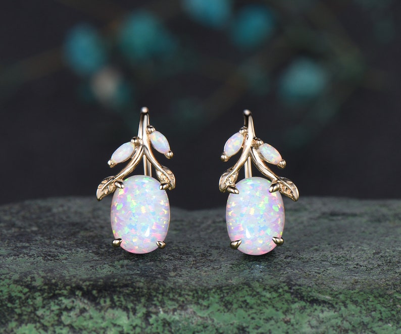 May include: A pair of gold earrings with white opal stones. Each earring features a delicate branch design with small opal accents.