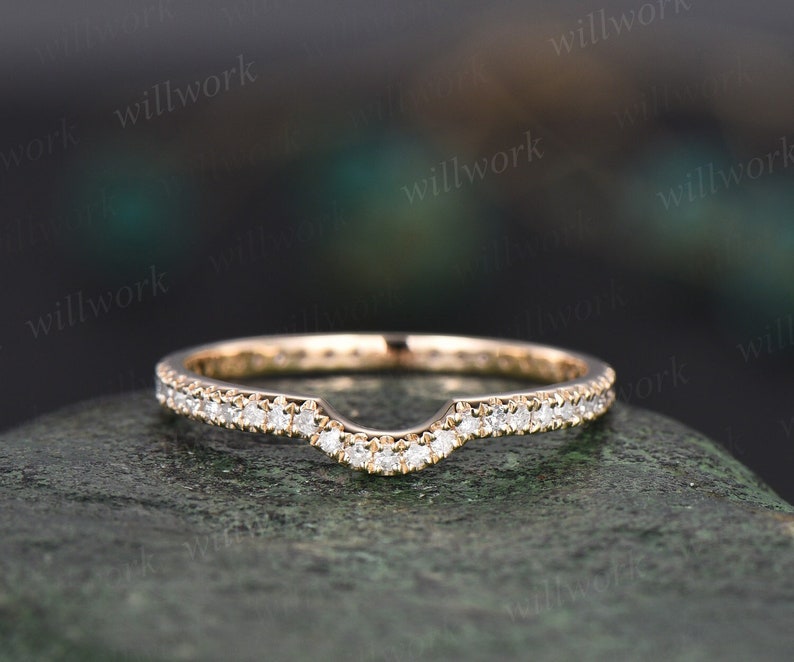 May include: A delicate, curved wedding band with a row of small, round diamonds set in a rose gold band.