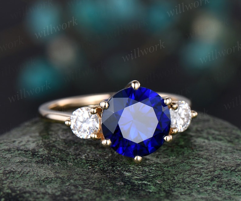 May include: A gold engagement ring with a large blue sapphire center stone and two smaller round diamonds on either side.