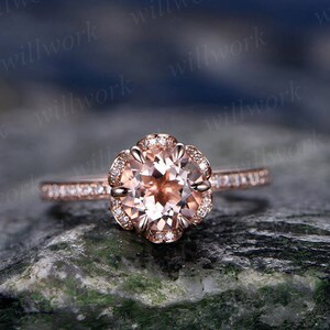 May include: A rose gold engagement ring with a round morganite center stone and a halo of smaller diamonds. The band is also set with smaller diamonds.