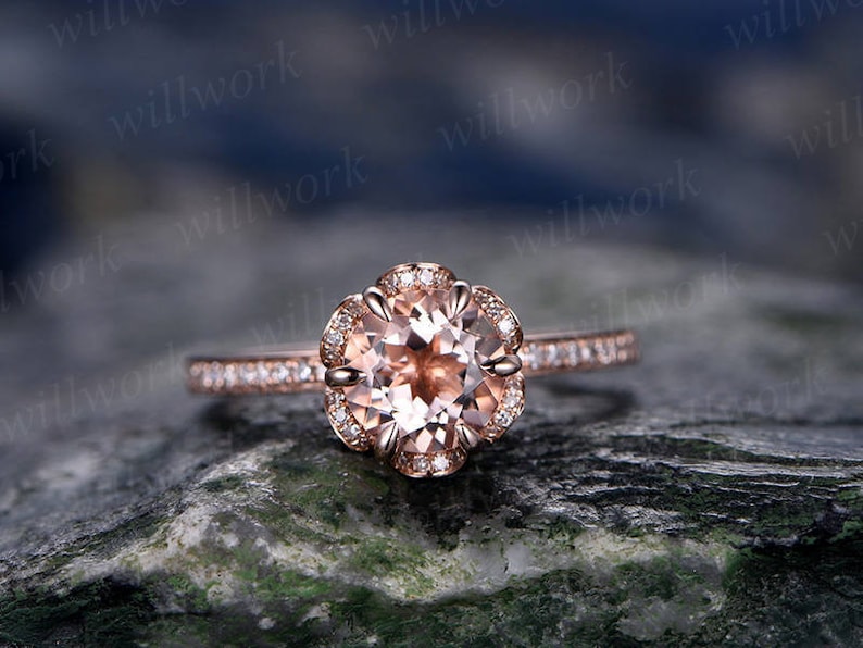 May include: A rose gold engagement ring with a round morganite center stone and a halo of smaller diamonds. The band is also set with smaller diamonds.