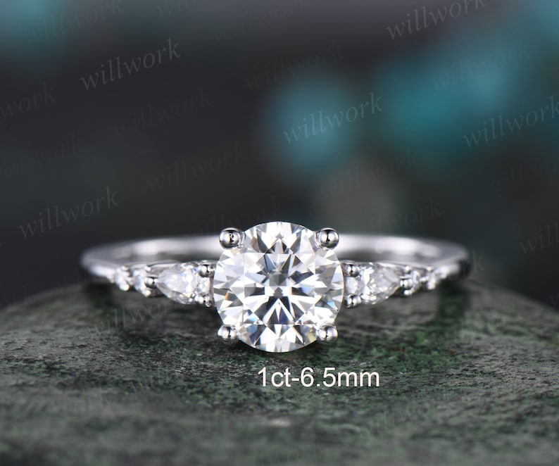 May include: A silver engagement ring with a round centre stone and three pear-shaped accent stones. The centre stone is 1ct-6.5mm.