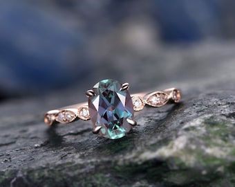 May include: A rose gold engagement ring with an oval-shaped green and blue gemstone surrounded by smaller diamonds. The ring is set on a delicate band with a decorative design.