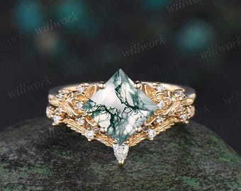 May include: A gold ring featuring a square green moss agate gemstone, surrounded by smaller diamonds. The ring has a delicate floral design.