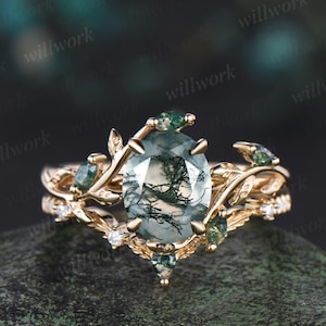 May include: A gold ring with a green moss agate gemstone set in a delicate leafy design. The ring features a band with smaller green gemstones and diamonds.