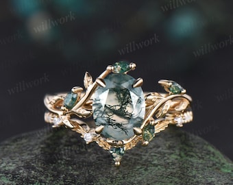 Op de afbeelding: Een gouden ring met een groene mosagaat-edelsteen gezet in een delicaat bladontwerp. De ring heeft een band met kleinere groene edelstenen en diamanten.
