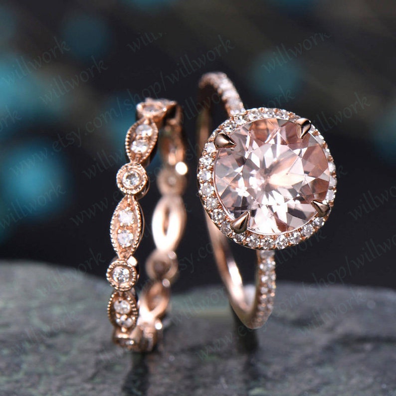 May include: A rose gold engagement ring set with a large round morganite center stone and a halo of smaller round diamonds. The ring is paired with a matching rose gold wedding band with a delicate design of round diamonds.