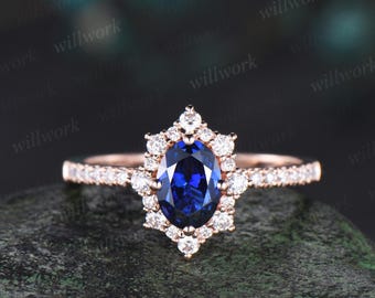 Op de afbeelding: Een verlovingsring van roségoud met een grote ovale blauwe saffier omringd door een halo van kleinere diamanten. De band is ook bezet met diamanten.