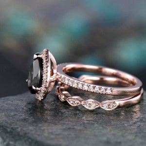 May include: A rose gold engagement ring set featuring a pear-shaped black gemstone, surrounded by small white gemstones. The set includes a matching band with small white gemstones and a decorative band.