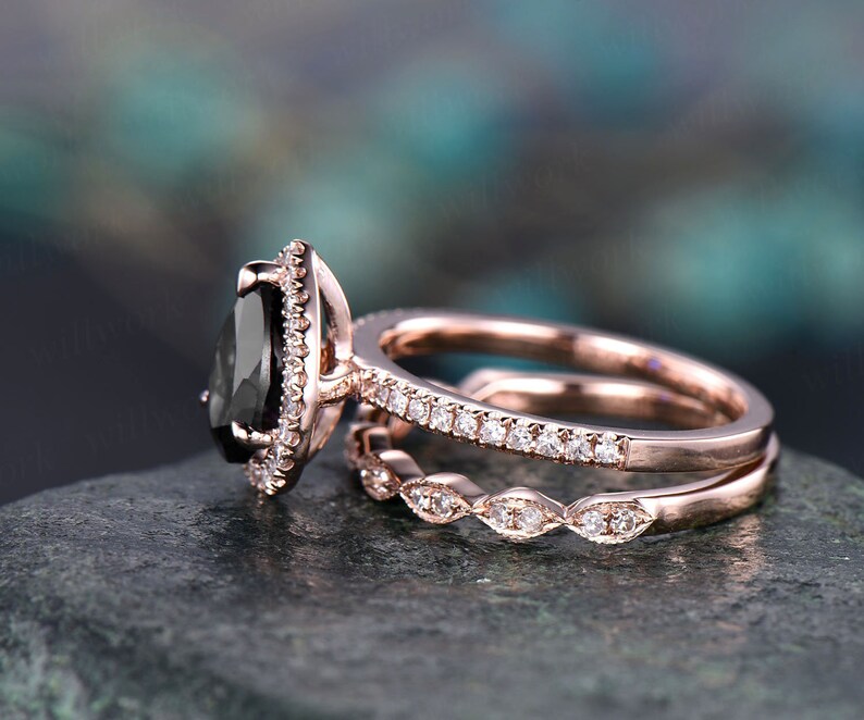 May include: A rose gold engagement ring set featuring a pear-shaped black gemstone, surrounded by small white gemstones. The set includes a matching band with small white gemstones and a decorative band.
