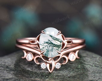 Könnte beinhalten: Ein Verlobungsring aus Roségold mit einem Moosachat-Mittelstück und einem zarten Band mit kleinen Diamanten. Der Ring liegt auf einer strukturierten Steinoberfläche.