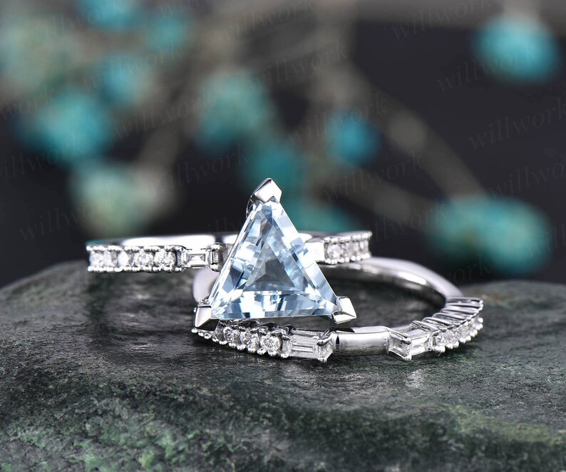 May include: A silver engagement ring set with a triangular aquamarine center stone and a matching band with smaller diamonds