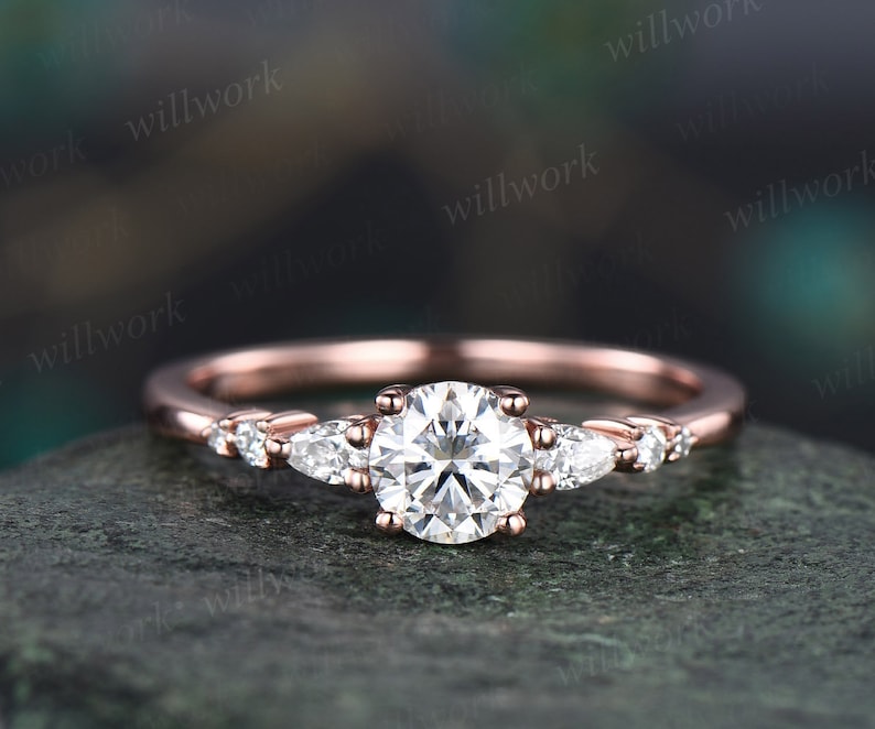May include: A rose gold engagement ring featuring a round centre stone and pear-shaped accent stones.