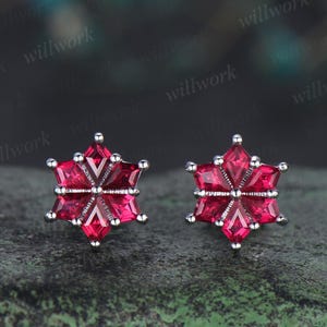 Puede incluir: Un par de pendientes en forma de copo de nieve con piedras de circonita cúbica rojas.