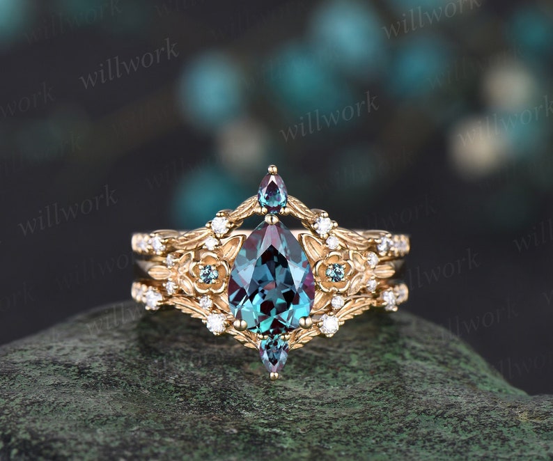 May include: A pear-shaped, teal blue gemstone ring with a gold band. The ring has a floral design with smaller gemstones and a delicate band.