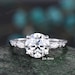 May include: A silver engagement ring featuring a large round centre stone and two pear-shaped accent stones. The centre stone is 2 carats and 8 millimetres in diameter. The ring is set on a silver band with small round stones.