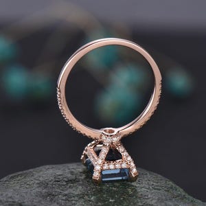 May include: A rose gold engagement ring with a square-shaped blue topaz gemstone surrounded by a halo of smaller diamonds. The ring band is also set with smaller diamonds.