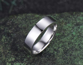 May include: A polished silver ring with a flat top and rounded edges. The ring reflects the surrounding environment, showcasing a smooth, shiny surface. The ring is set against a mottled green background.