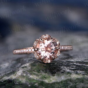 May include: A rose gold engagement ring with a round morganite center stone and a halo of smaller diamonds. The band is also set with smaller diamonds.
