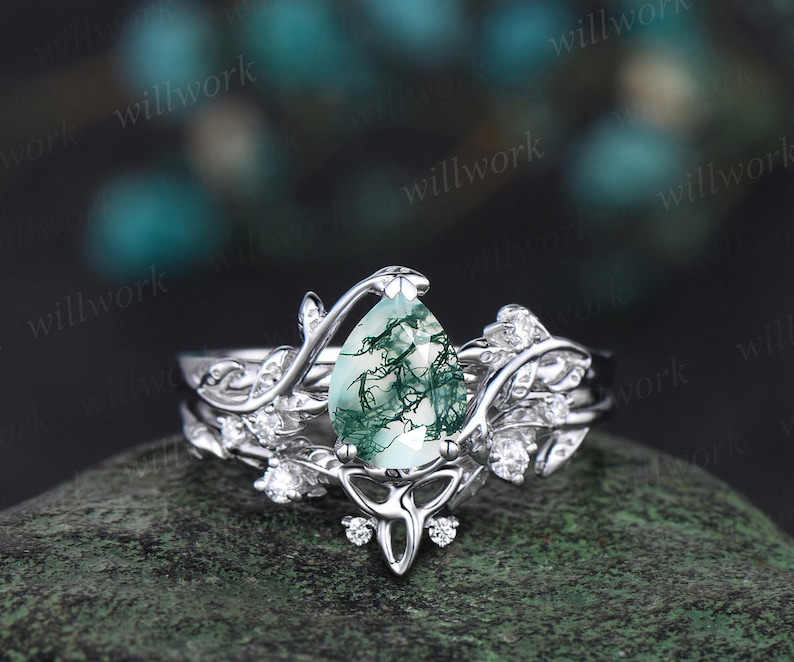 May include: A pear-shaped green moss agate engagement ring set in a silver band with a delicate leaf design. The ring is set with smaller diamonds on the band and on the leaf design.